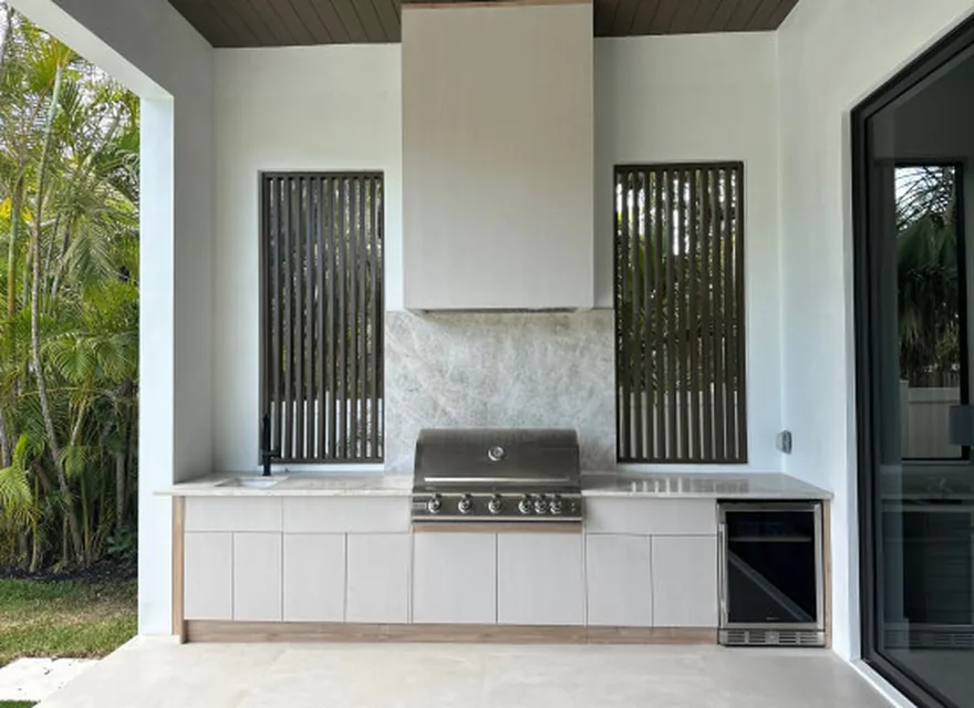 Covered patio outdoor kitchen with grill, hood, beverage refrigeration, and light slab cabinetry.